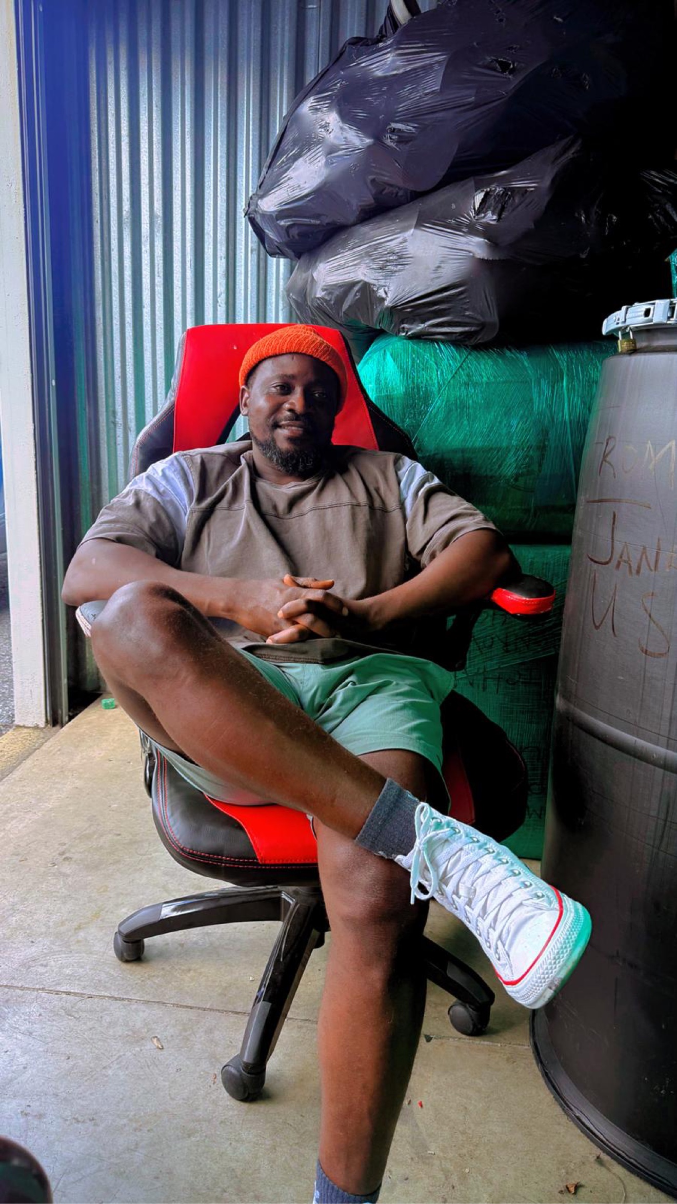 CEO Abraham A. Manobah seated in front of wrapped customer cargo and a shipping barrel